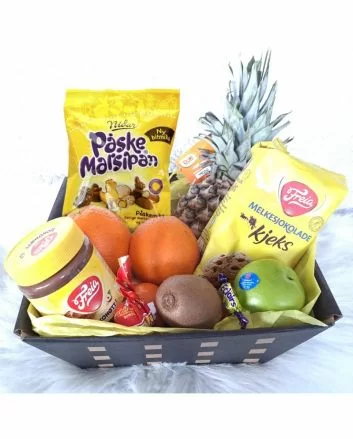 På bildet ser vi en stilren pappkurv med frisk frukt – ananas, appelsin, eple og kiwi – sammen med klassisk påskegodteri som påskemarsipan, melkesjokolade og sjokonøtt.